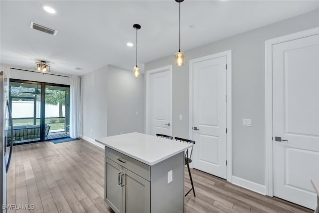 kitchen with visible vents, light wood finished floors, a breakfast bar, gray cabinets, and light countertops