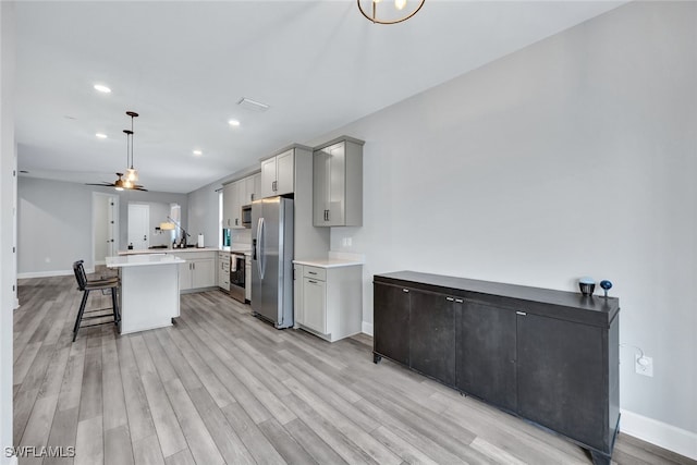 kitchen featuring stainless steel fridge with ice dispenser, gray cabinetry, light countertops, a kitchen bar, and light wood-type flooring