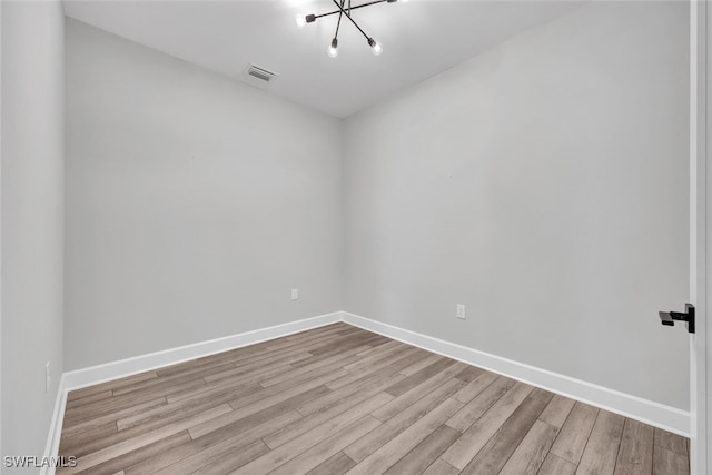 empty room featuring a notable chandelier, visible vents, baseboards, and wood finished floors