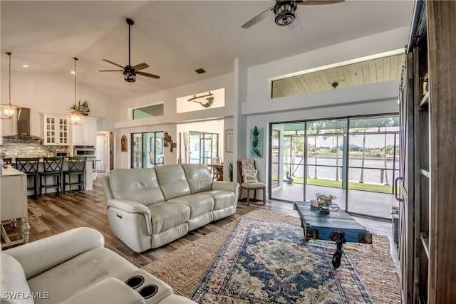 living room featuring ceiling fan with notable chandelier, dark wood-type flooring, and vaulted ceiling