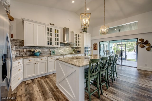 kitchen with white cabinets, wall chimney exhaust hood, stainless steel fridge with ice dispenser, and a kitchen island with sink