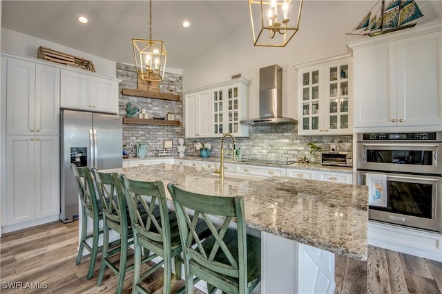 kitchen with backsplash, white cabinetry, wall chimney range hood, and appliances with stainless steel finishes