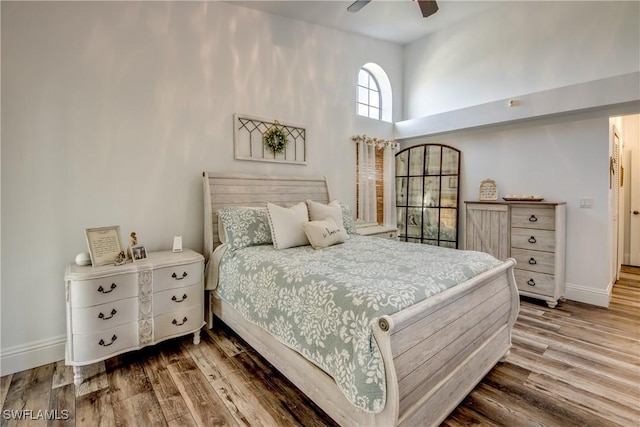 bedroom featuring hardwood / wood-style flooring, ceiling fan, and a towering ceiling