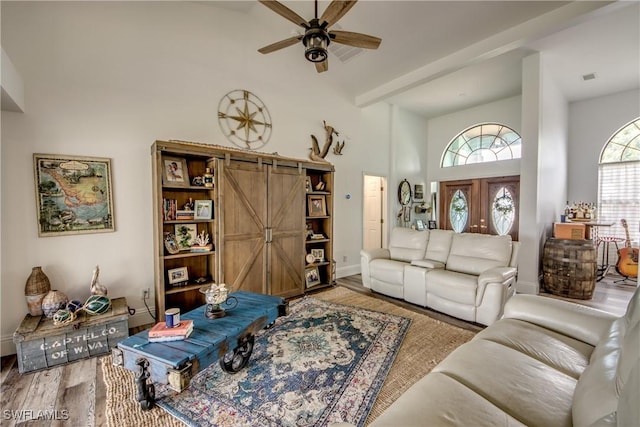 living room with hardwood / wood-style flooring, ceiling fan, a barn door, and a towering ceiling