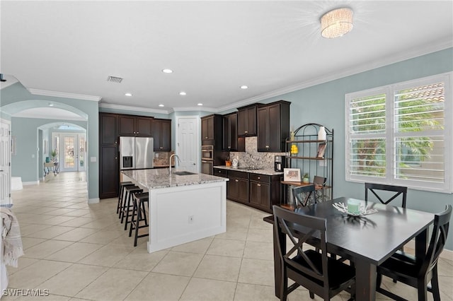 kitchen featuring light tile patterned flooring, sink, tasteful backsplash, a center island with sink, and light stone countertops