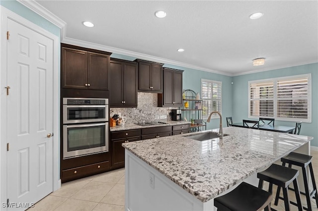 kitchen with dark brown cabinetry, sink, a kitchen breakfast bar, stainless steel double oven, and a kitchen island with sink