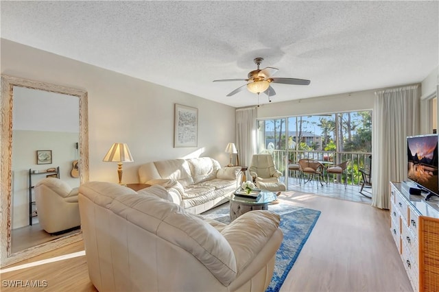 living room with ceiling fan, light wood-type flooring, and a textured ceiling