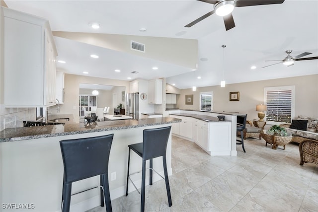 kitchen with lofted ceiling, dark stone counters, kitchen peninsula, stainless steel fridge, and white cabinetry