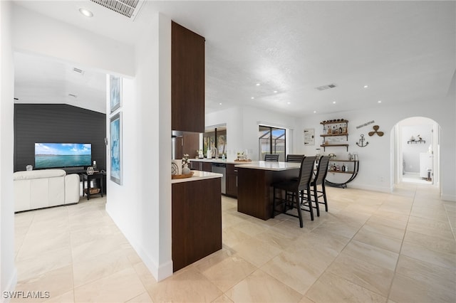 kitchen with a breakfast bar, dishwasher, dark brown cabinets, a kitchen island, and light tile patterned flooring