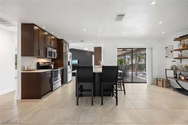 kitchen featuring dark brown cabinetry, light tile patterned floors, appliances with stainless steel finishes, a kitchen breakfast bar, and ceiling fan