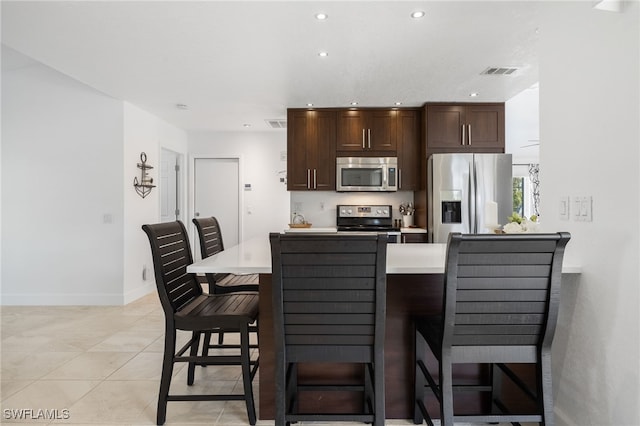 kitchen featuring light tile patterned flooring, stainless steel appliances, a kitchen breakfast bar, and dark brown cabinets