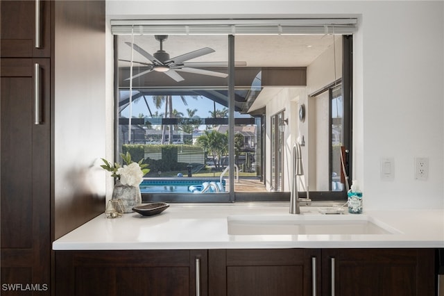 bar with dark brown cabinetry, sink, and ceiling fan