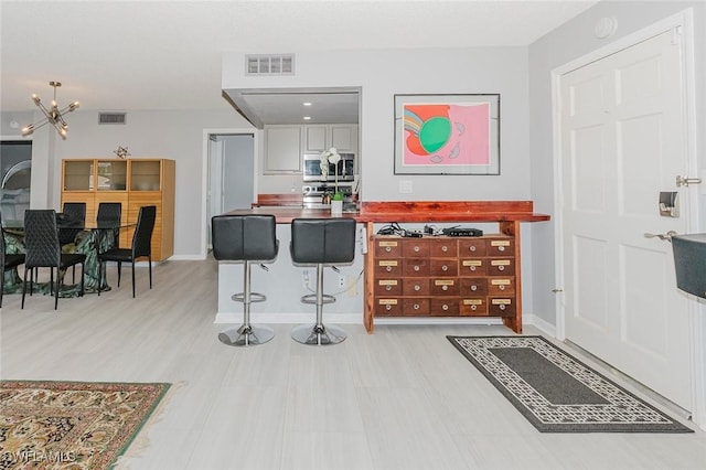 2600 Gulf Shore Blvd N Unit 32, Naples, FL 34103 - kitchen featuring stainless steel microwave, white cabinetry, a kitchen breakfast bar, light wood-style floors, and a chandelier