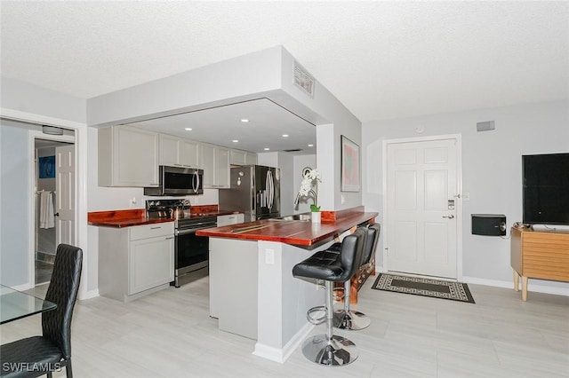 kitchen featuring a breakfast bar, white cabinets, a textured ceiling, appliances with stainless steel finishes, and kitchen peninsula