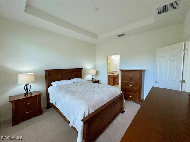 bedroom featuring connected bathroom, light colored carpet, and a raised ceiling