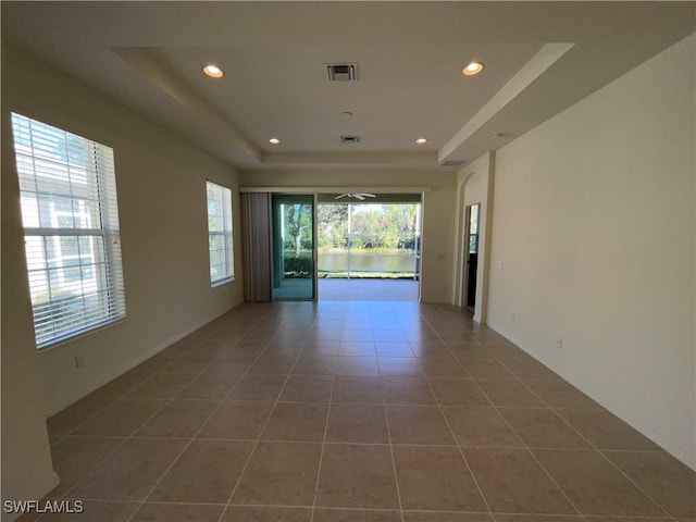 tiled spare room featuring a raised ceiling and ceiling fan