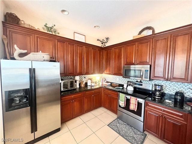 kitchen with light tile patterned flooring, backsplash, stainless steel appliances, and dark stone countertops