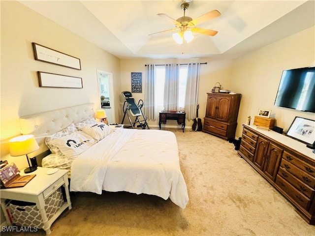 bedroom featuring ceiling fan, a raised ceiling, and light carpet