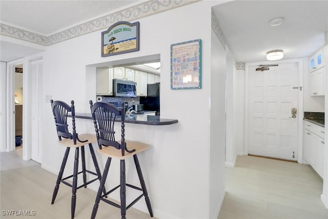 kitchen with black refrigerator, backsplash, white cabinetry, and light hardwood / wood-style floors