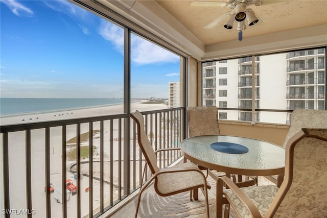 unfurnished sunroom with ceiling fan, a water view, and a beach view