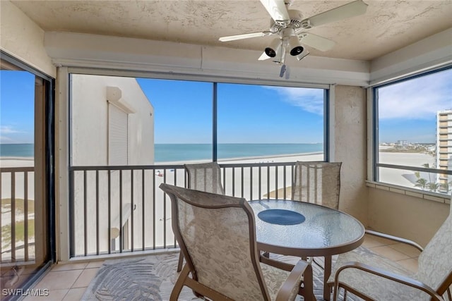 sunroom / solarium featuring ceiling fan, a water view, and a view of the beach