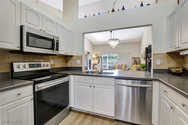 kitchen featuring a notable chandelier, light wood-type flooring, white cabinetry, and appliances with stainless steel finishes