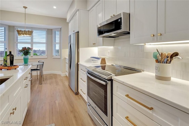 kitchen with pendant lighting, tasteful backsplash, white cabinets, stainless steel appliances, and light stone countertops