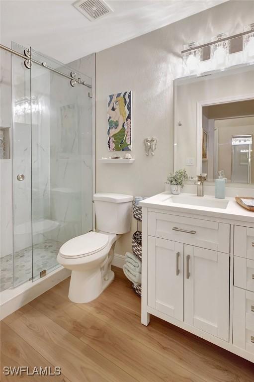 bathroom featuring vanity, hardwood / wood-style flooring, a shower with shower door, and toilet