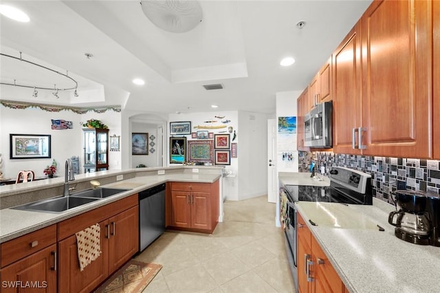 kitchen with sink, tasteful backsplash, kitchen peninsula, a tray ceiling, and appliances with stainless steel finishes