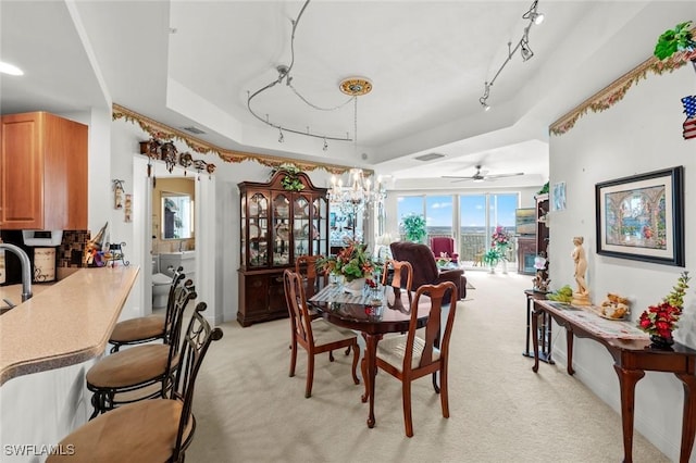 dining space with ceiling fan with notable chandelier, light carpet, and a tray ceiling