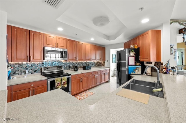 kitchen with backsplash, stainless steel appliances, a tray ceiling, sink, and light tile patterned flooring