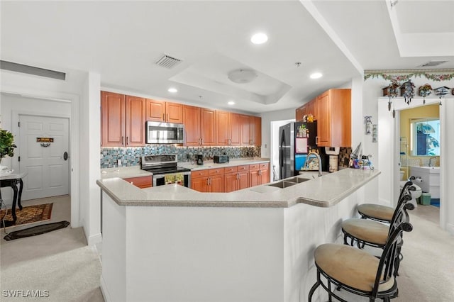 kitchen with kitchen peninsula, a kitchen bar, stainless steel appliances, a raised ceiling, and sink