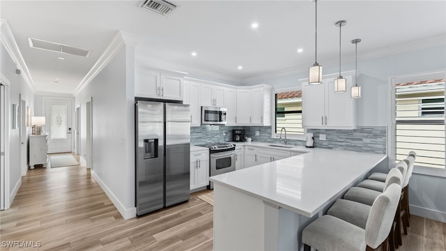 kitchen with white cabinetry, kitchen peninsula, pendant lighting, a breakfast bar, and appliances with stainless steel finishes