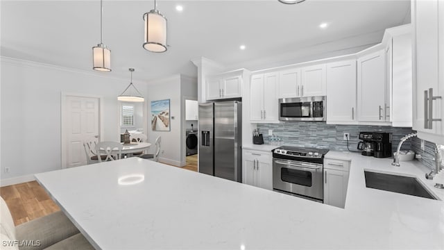 kitchen with pendant lighting, sink, appliances with stainless steel finishes, white cabinetry, and washer / clothes dryer