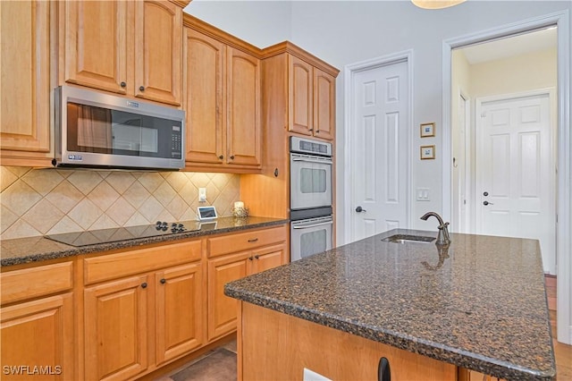 kitchen with dark stone countertops, a kitchen island with sink, stainless steel appliances, sink, and tasteful backsplash