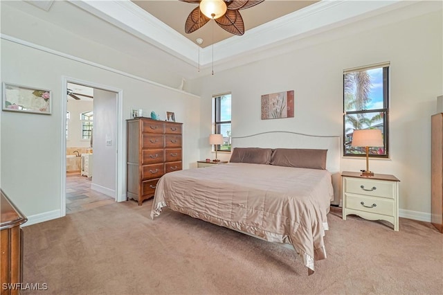 bedroom featuring ensuite bath, light colored carpet, a tray ceiling, ornamental molding, and ceiling fan