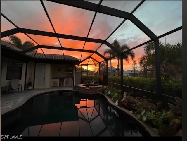 pool at dusk with glass enclosure, an in ground hot tub, and a patio area