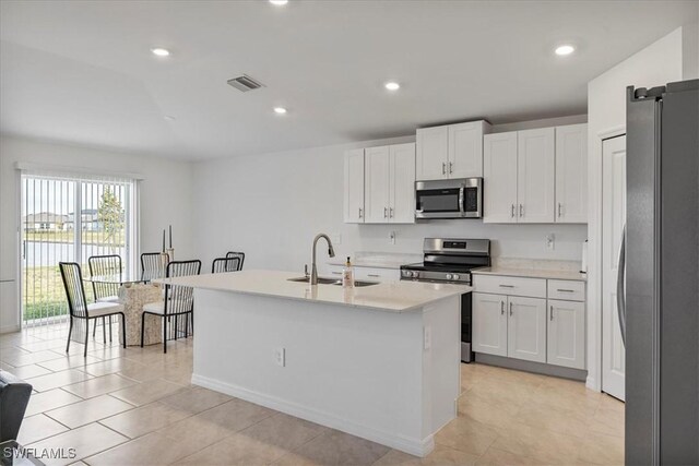 kitchen with appliances with stainless steel finishes, sink, light tile patterned floors, white cabinets, and an island with sink