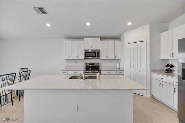 kitchen featuring white cabinetry, a kitchen island with sink, light stone countertops, and appliances with stainless steel finishes