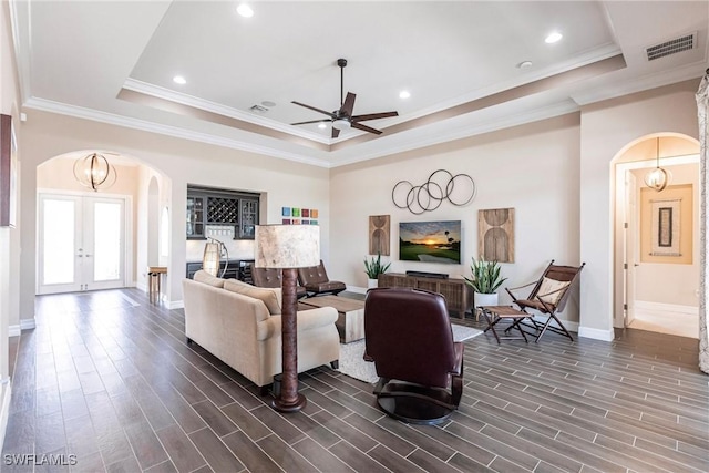 living room with ceiling fan, ornamental molding, a tray ceiling, and french doors