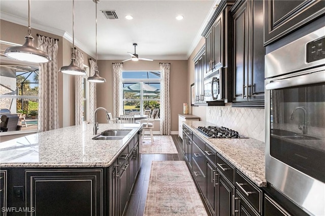 kitchen featuring pendant lighting, backsplash, a kitchen island with sink, sink, and stainless steel appliances