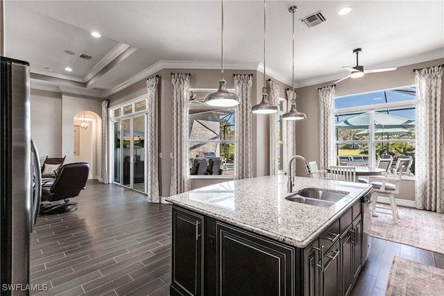 kitchen with light stone countertops, sink, ceiling fan, hanging light fixtures, and a center island with sink