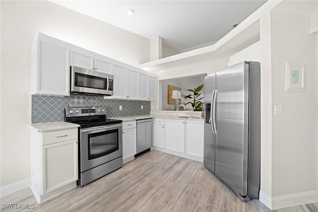 kitchen featuring decorative backsplash, light wood-type flooring, appliances with stainless steel finishes, light stone counters, and white cabinetry