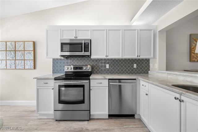 kitchen with tasteful backsplash, light stone counters, stainless steel appliances, vaulted ceiling, and white cabinetry