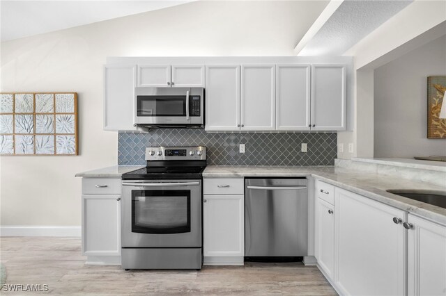 13120 Castle Harbour Dr Unit N4, Naples, FL 34110 - kitchen featuring appliances with stainless steel finishes, decorative backsplash, light wood-style flooring, light stone countertops, and lofted ceiling