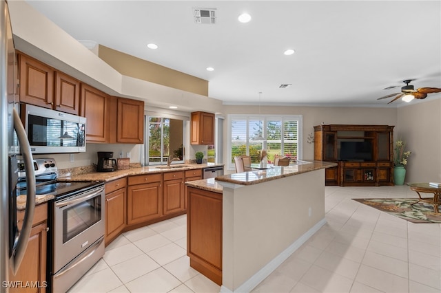 kitchen with light tile patterned flooring, ceiling fan, appliances with stainless steel finishes, a kitchen island, and light stone counters