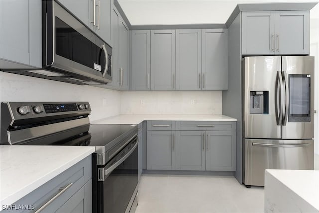 kitchen with stainless steel appliances, light stone counters, and gray cabinetry