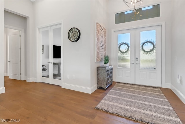 foyer entrance with a towering ceiling, wood-type flooring, and french doors