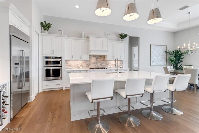 kitchen with sink, hanging light fixtures, an island with sink, appliances with stainless steel finishes, and white cabinetry