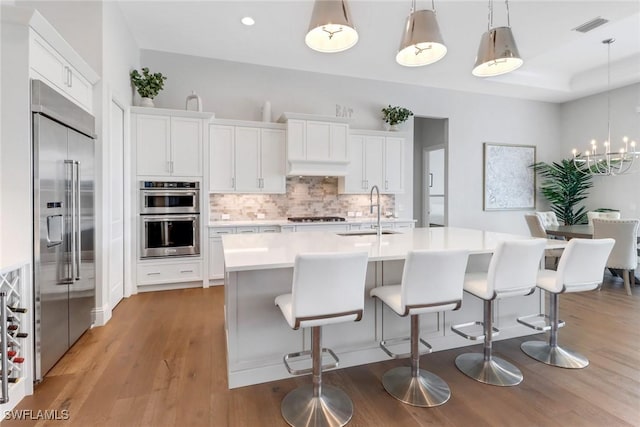 kitchen featuring stainless steel appliances, light countertops, white cabinetry, pendant lighting, and a sink